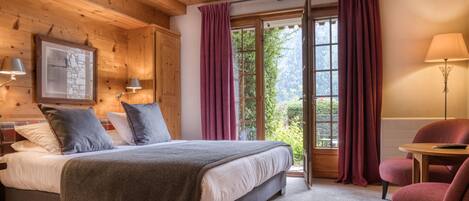 A bedroom with a bed, a chair, a table, and a window with curtains.