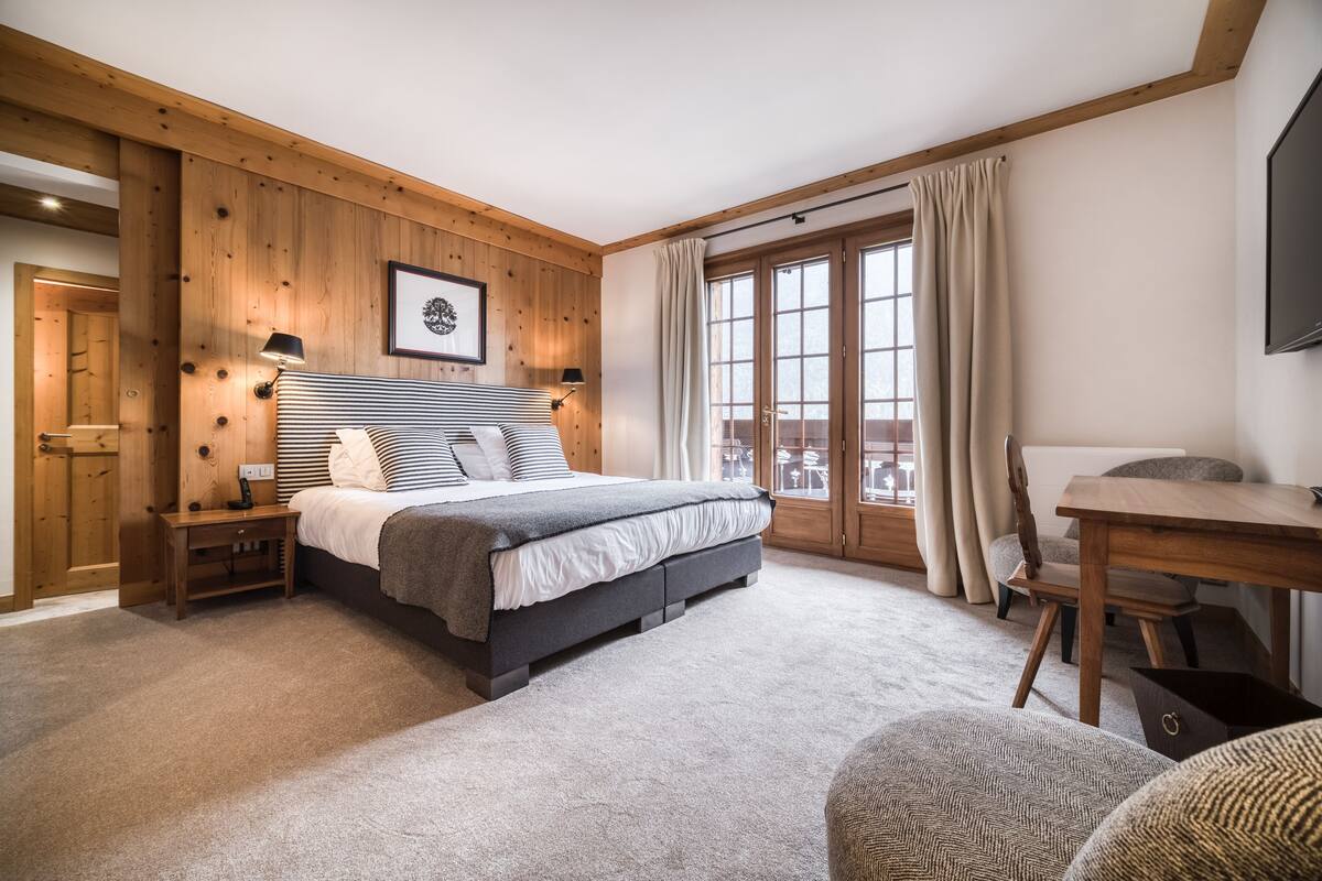 A bedroom with a large bed, wooden paneling, a desk, and a chair.