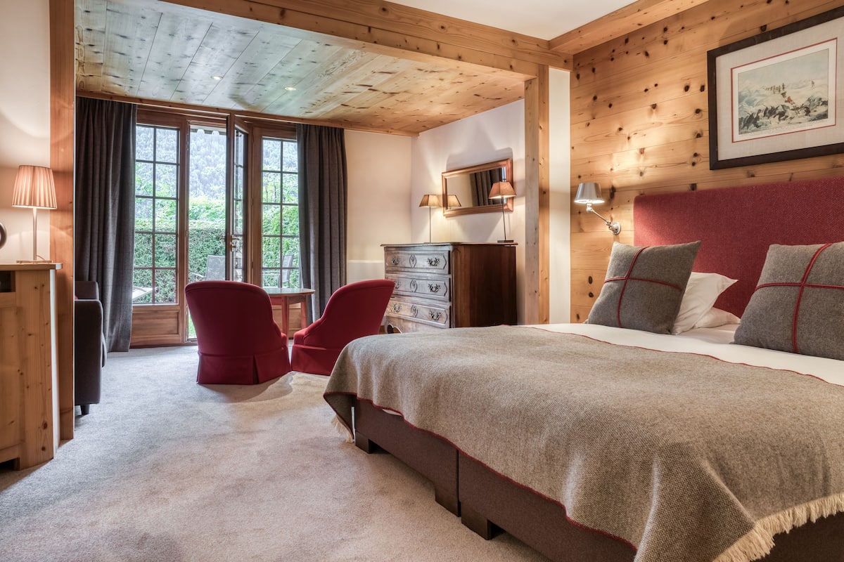 A bedroom with a large bed, a red chair, a dresser, and a window with curtains.