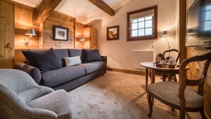 A cozy living room with a sofa, armchair, wooden beams, and a dining table with chairs. - Auberge du Bois Prin (Chamonix-Mont-Blanc)