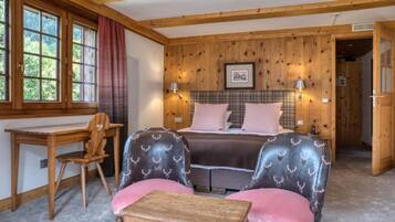 A cozy room with a bed, two upholstered chairs, a wooden desk, and a small table.
