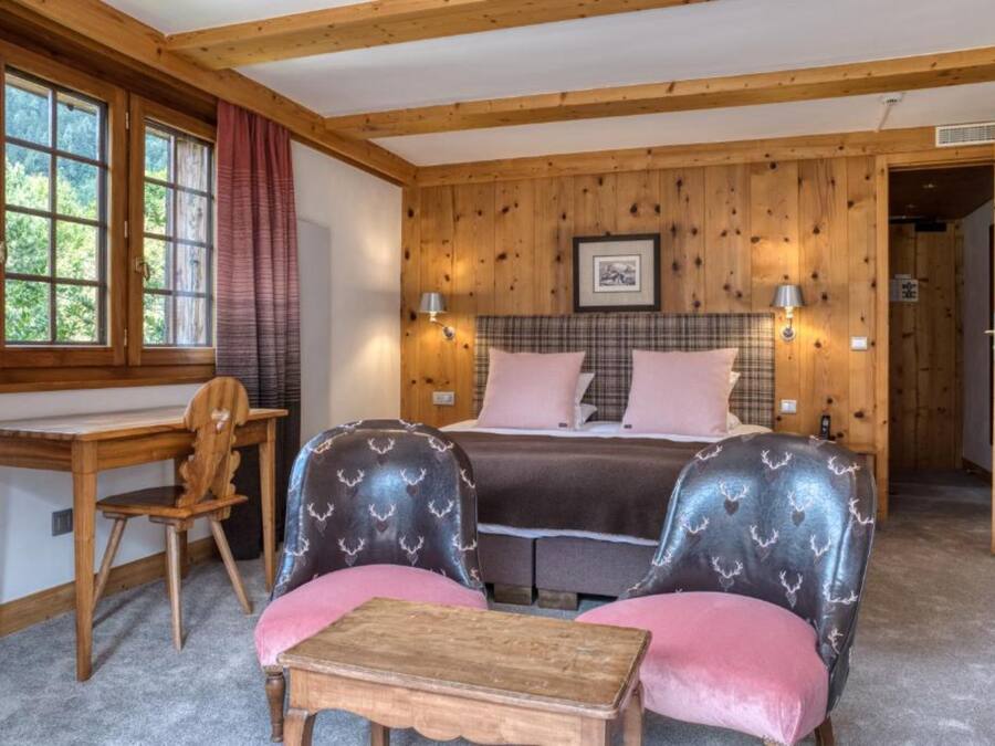 A cozy room with a bed, two upholstered chairs, a wooden desk, and a small table.