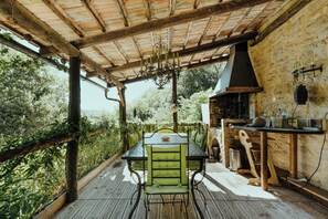 A covered outdoor dining area with a table and chairs, a hanging light fixture, and a stone wall.