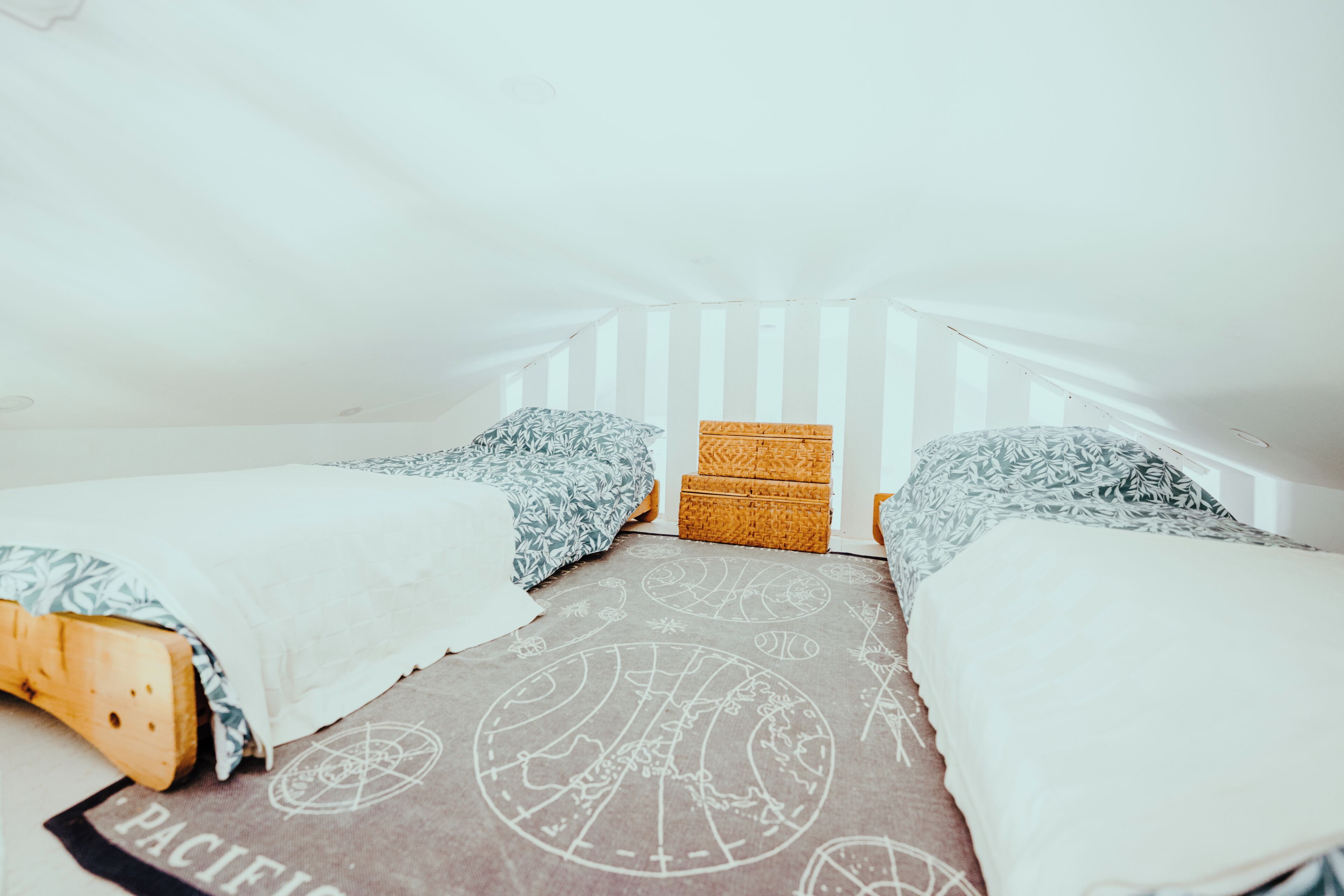 Ein kleines, dreieckiges Schlafzimmer im Dachgeschoss mit zwei Einzelbetten, einer gewebten Truhe und einem gemusterten Teppich.