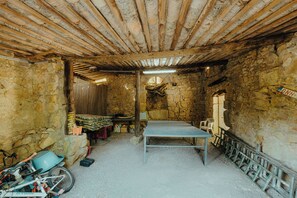 A rustic stone room with a wooden ceiling, a metal table, and a bicycle.