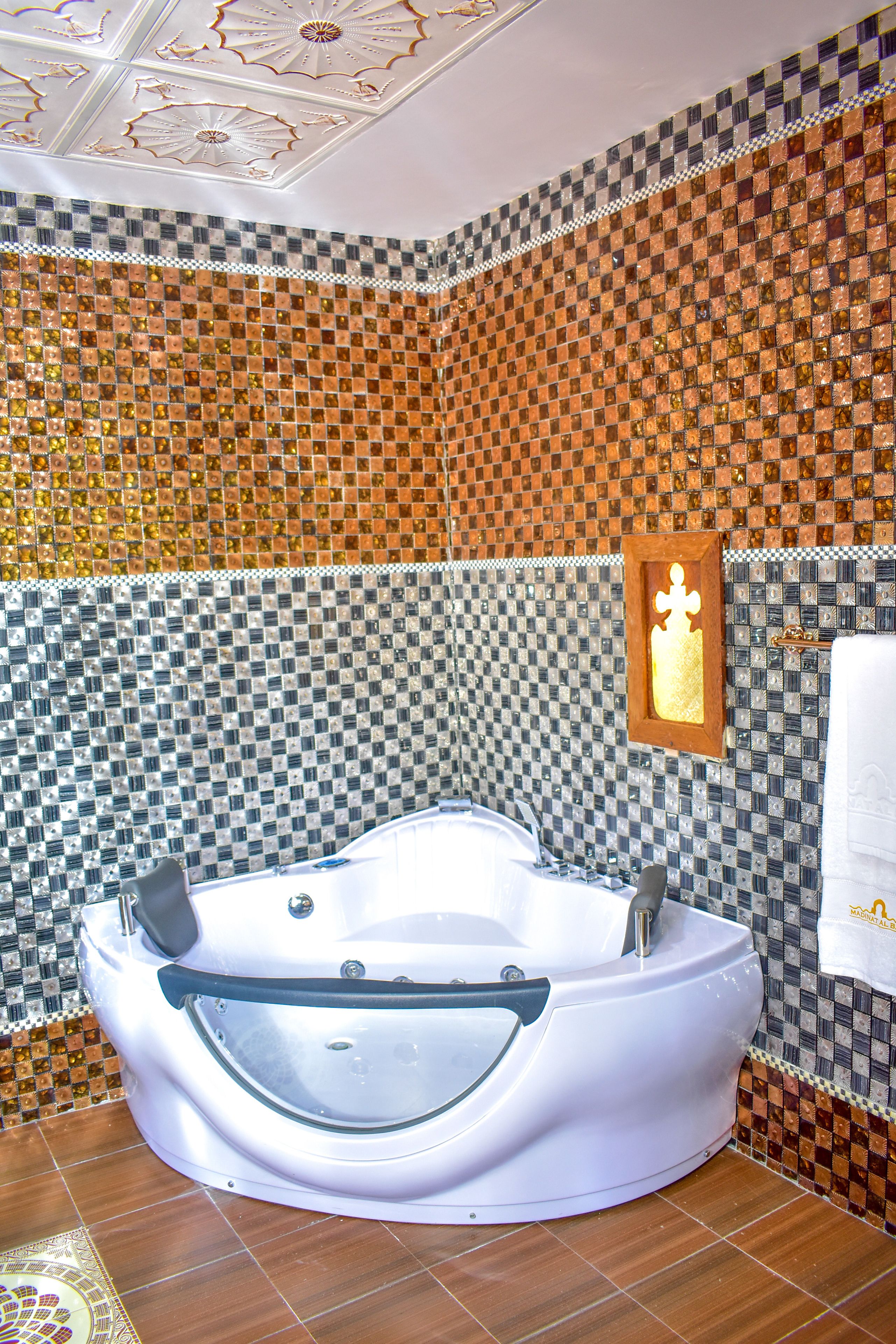 Un baño con una bañera grande, paredes de mosaico y un cuadro en la pared.