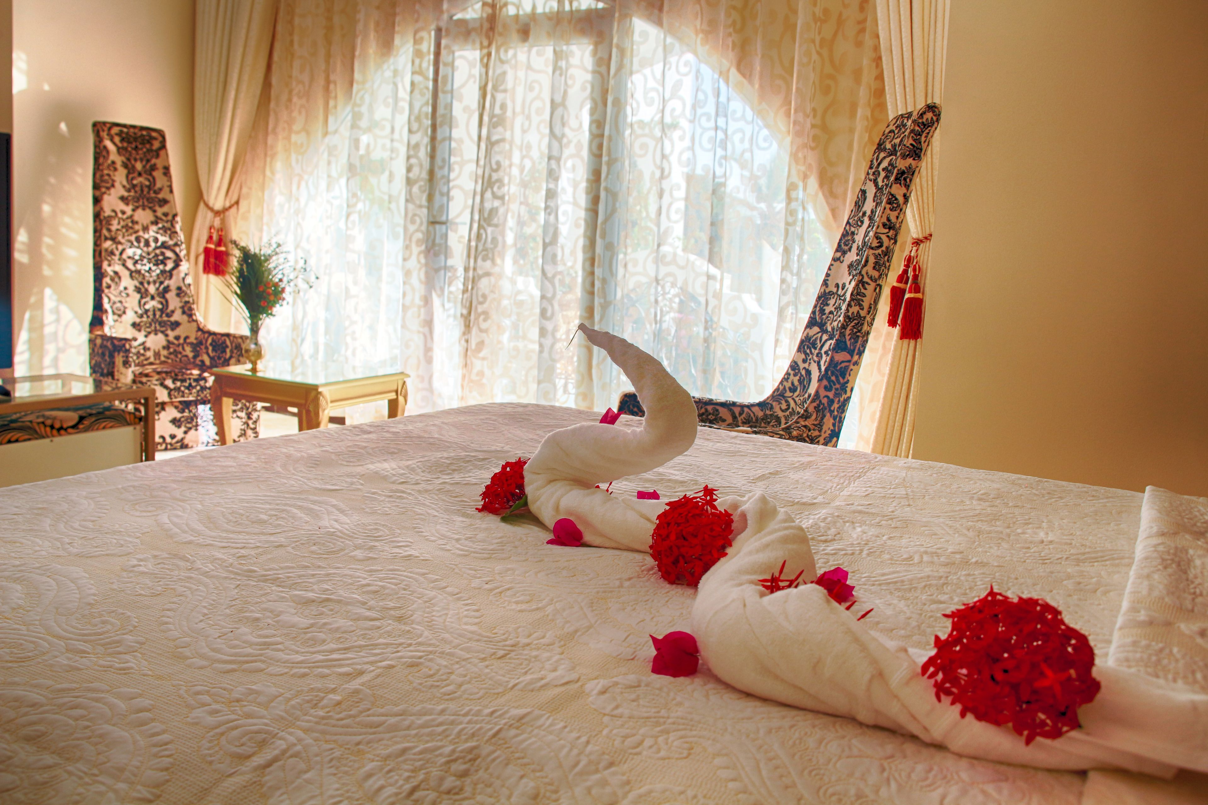 A bed with swan-shaped pillows and red flowers.