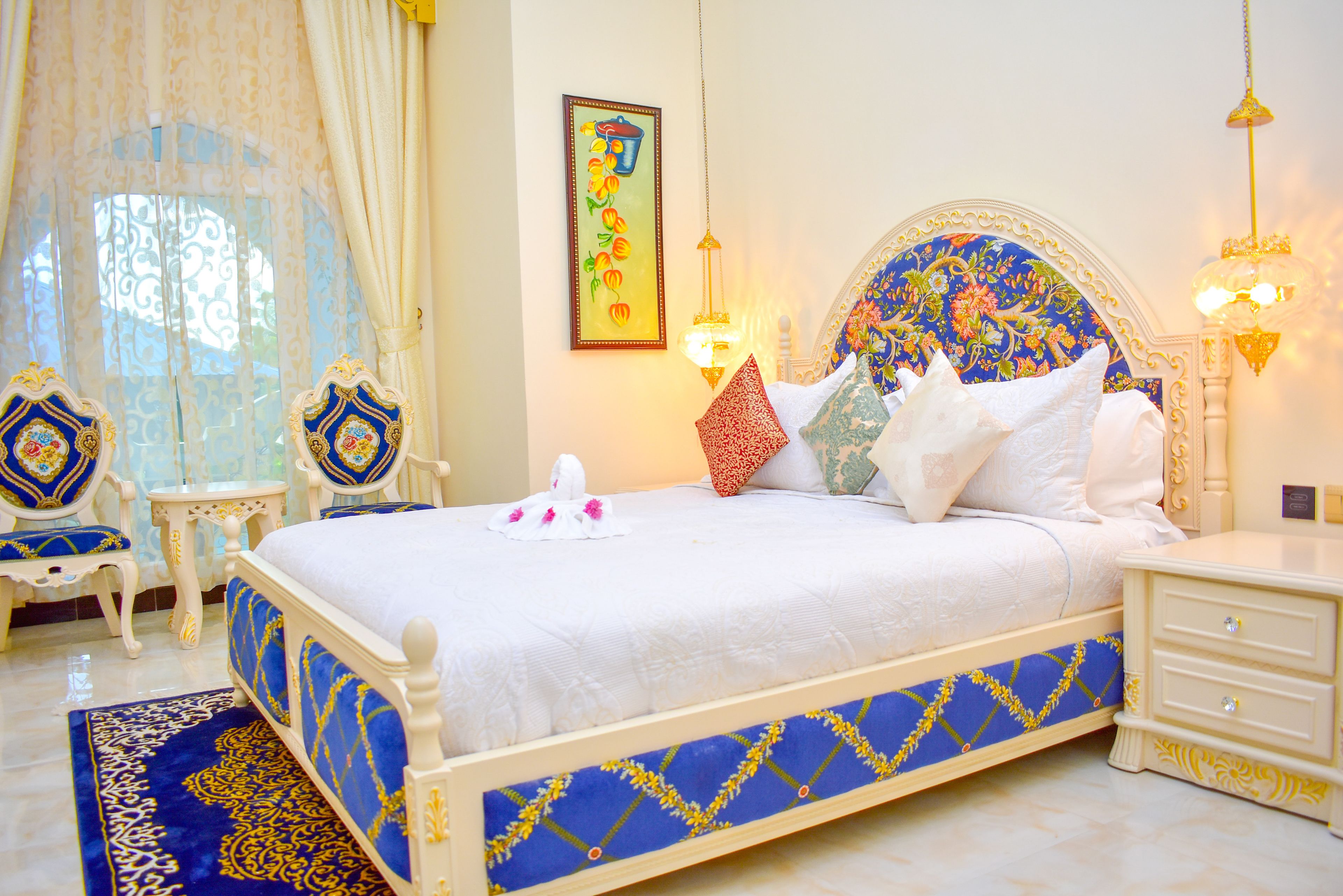 Uma cama com colcha azul e branca, um painel de cabeceira decorativo e uma mesa de cabeceira com abajur.