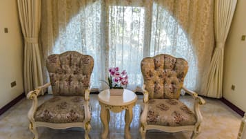 Two ornate armchairs with floral upholstery, a small round table, and a vase of flowers.