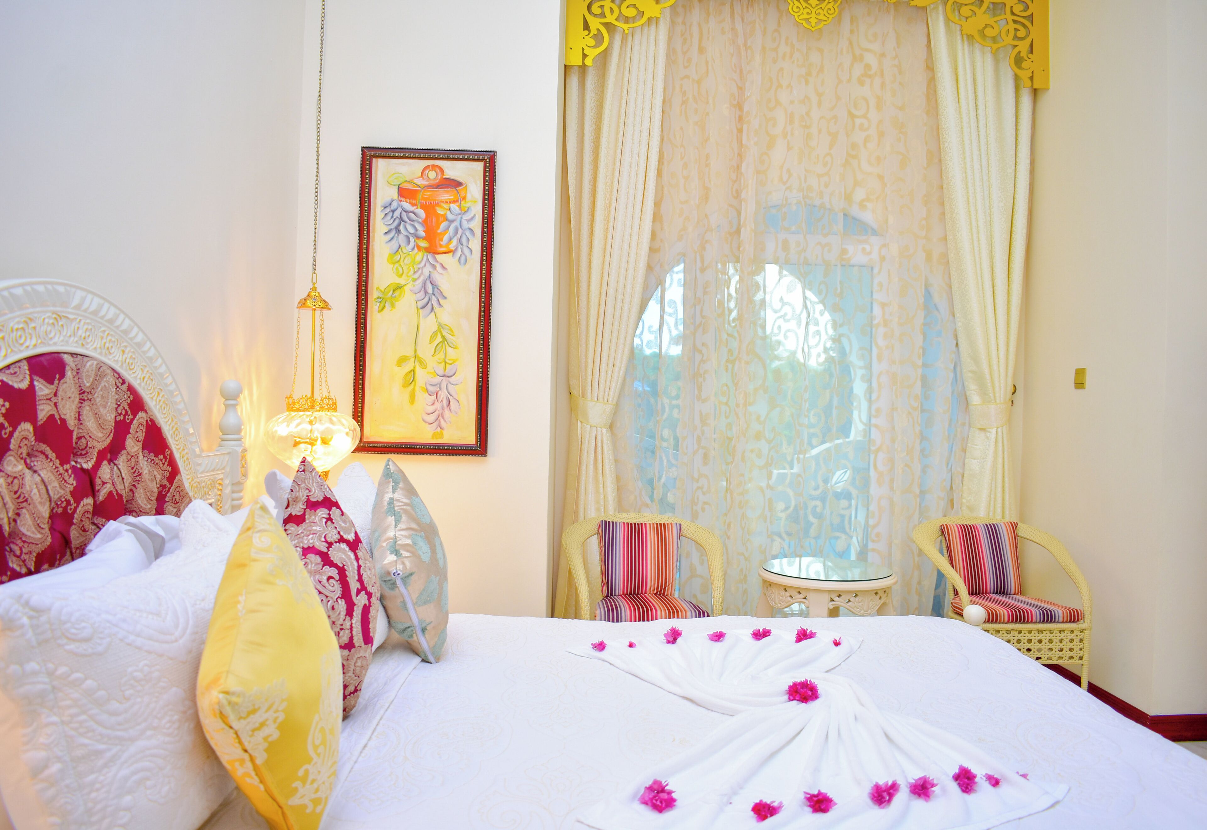 A hotel room with a bed, two chairs, a small table, and a window with curtains.