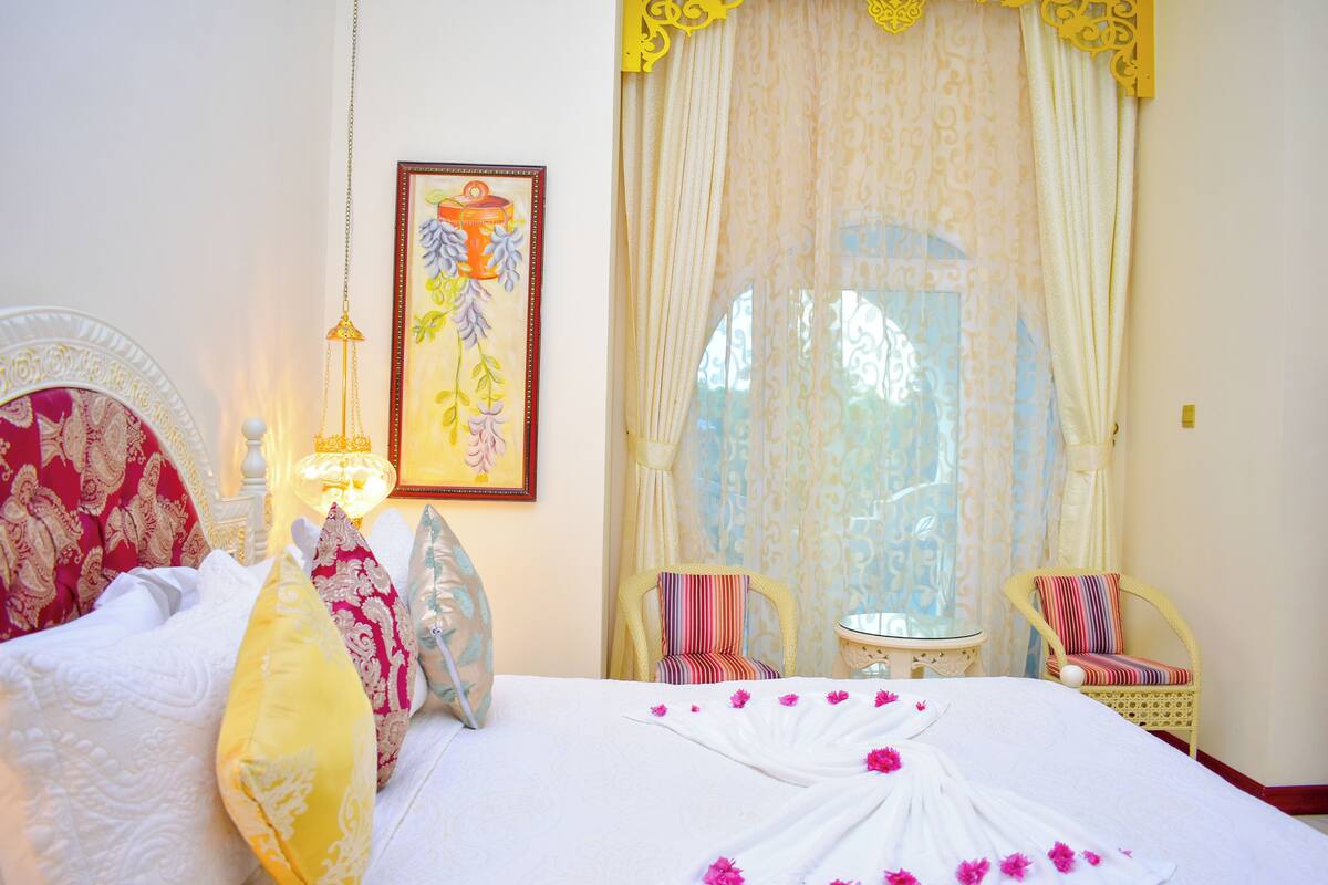 Une chambre d’hôtel avec un lit, deux chaises, une petite table et une fenêtre avec des rideaux.
