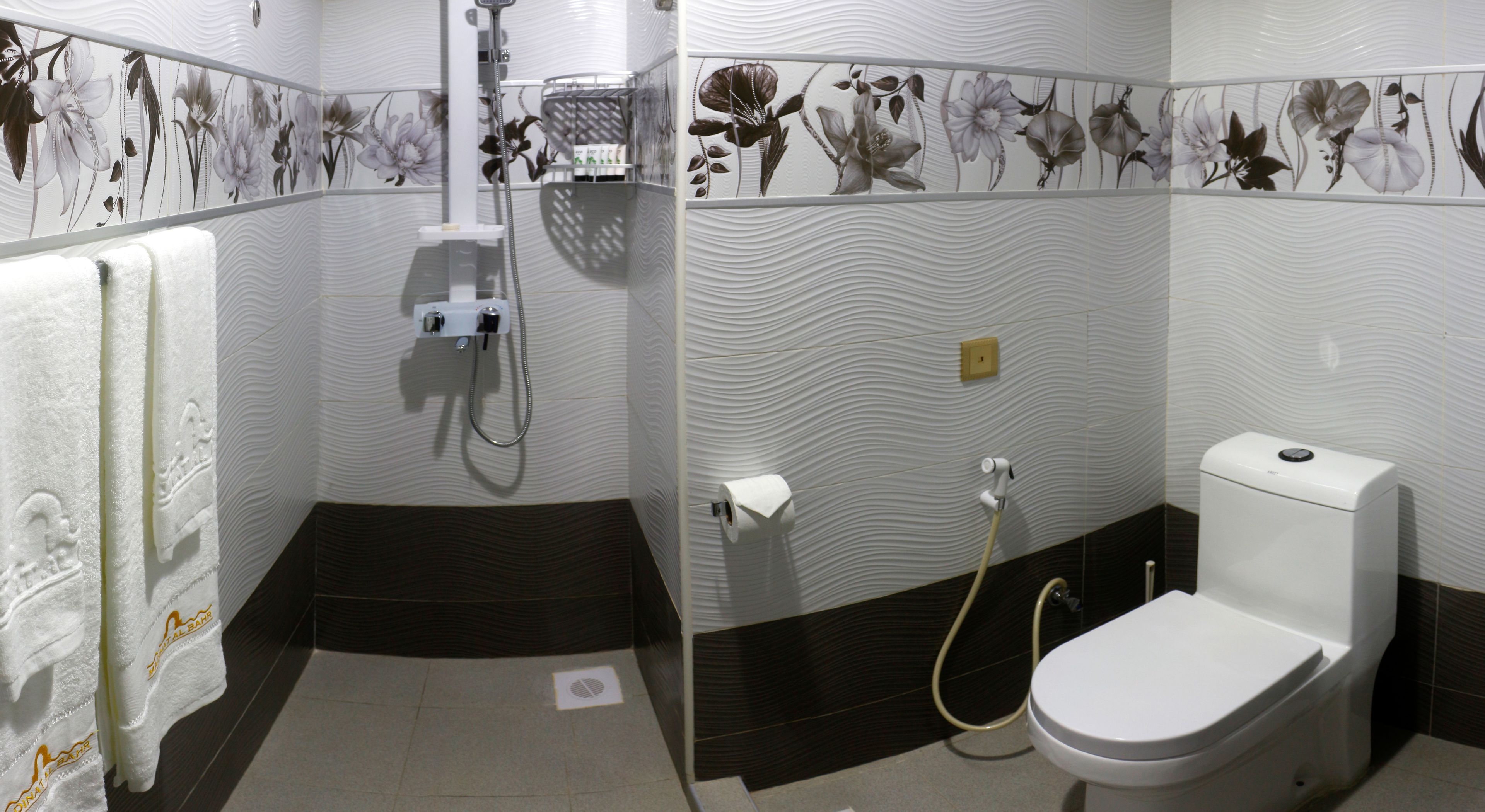 Un baño con inodoro, ducha y perchero para toallas.
