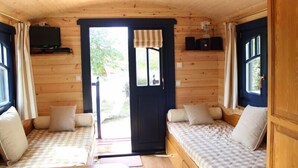 Ein gemütliches Blockhaus-Interieur mit zwei Holzbetten, einem Fernseher und einer zur Außenwelt führenden Tür.