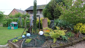 Um jardim com canteiros elevados, um parquinho e diversas plantas e flores.