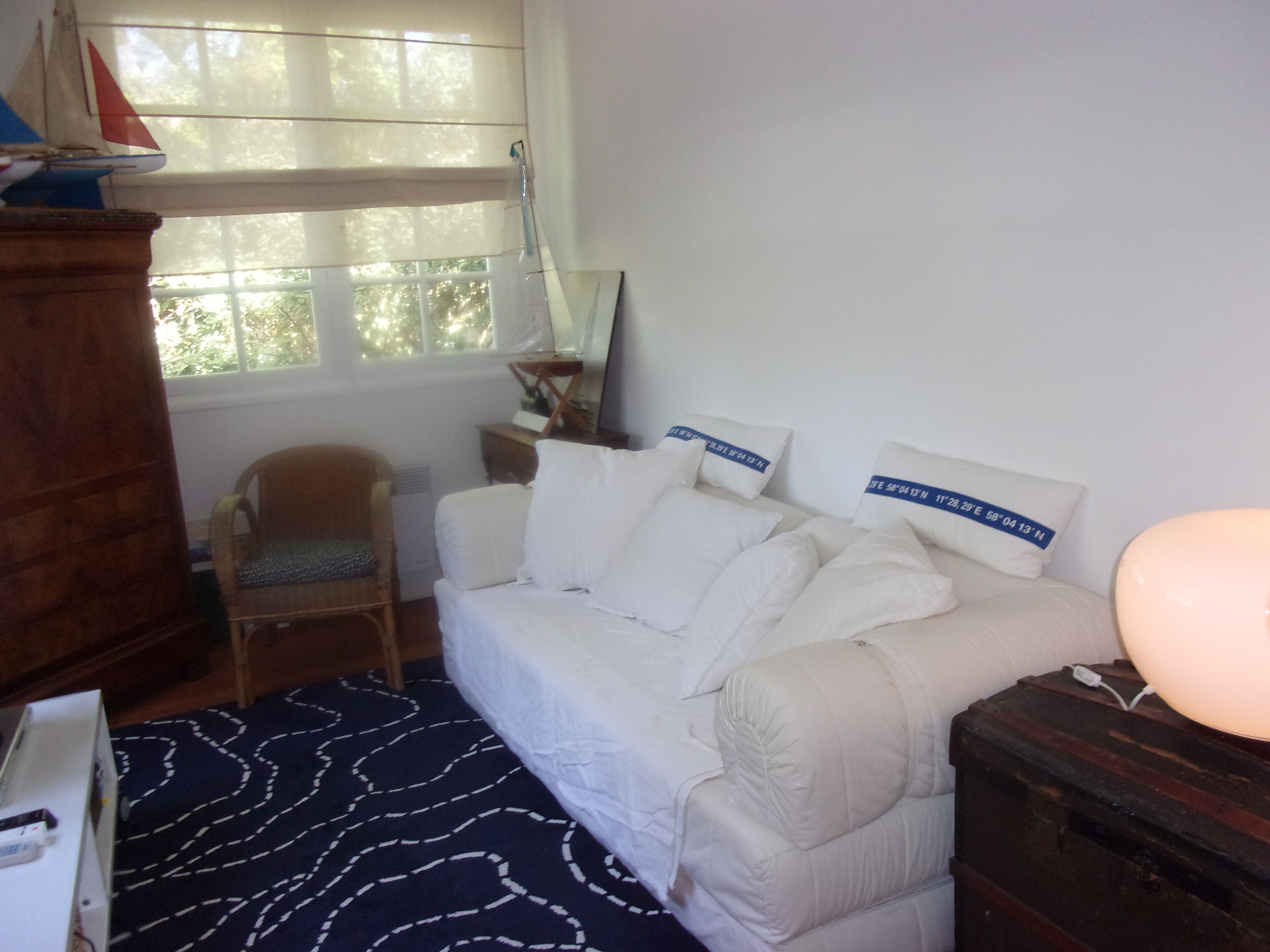 A room with a white sofa, a wooden chair, a patterned rug, a wooden cabinet, and a window with blinds.