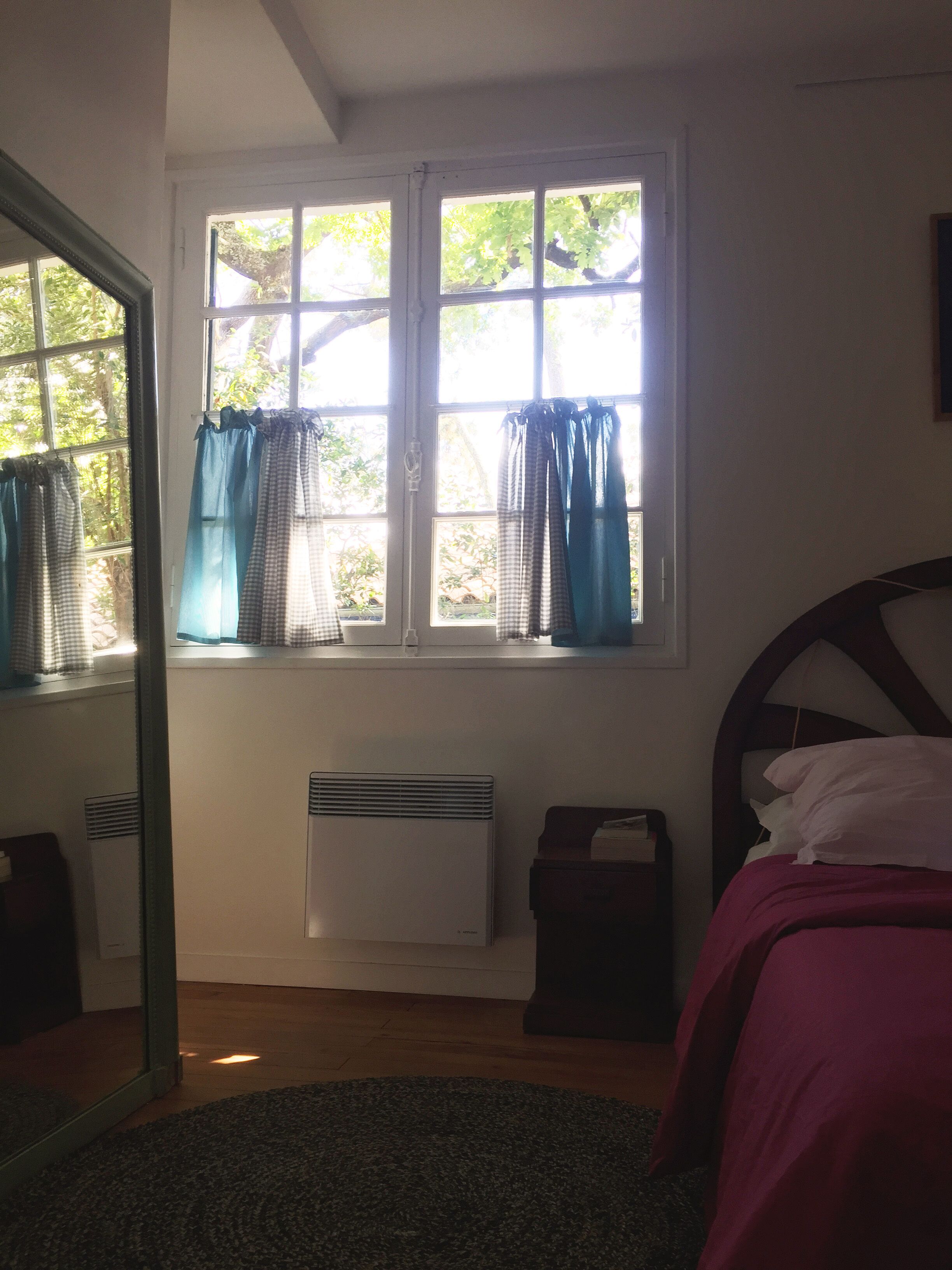 A bedroom with a bed, a window with curtains, a radiator, and a door.