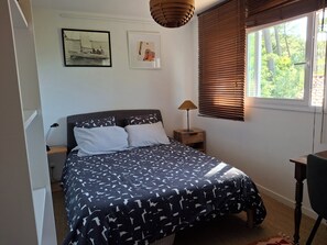 Un dormitorio con una cama, una mesita de noche, una lámpara, una ventana con persianas y una obra de arte en la pared.