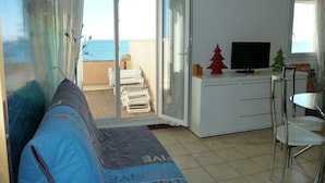 Ett rum med en soffa, en tv, ett litet bord och en balkong med utsikt över havet.
