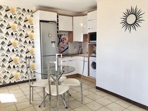 Une cuisine compacte équipée d’un réfrigérateur, d’un lave-linge et d’une table en verre avec des chaises.