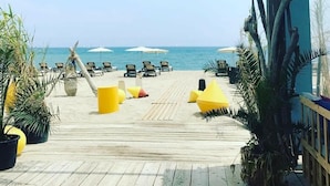 Ett avslappningsområde vid stranden med solstolar och parasoller, ett trädäck och utsikt över havet.