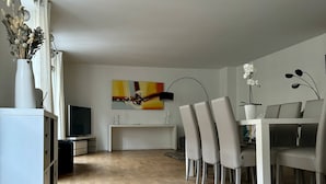 Moderni ruokailutila, jossa on puulattia, valkoiset huonekalut ja taulu seinällä.