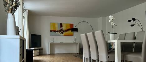 Uma sala de jantar moderna com piso de madeira, mobiliário branco e um quadro na parede.