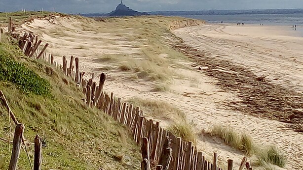 Ein Sandstrand mit einer Holzzaun und einer entfernten Hügelkette.