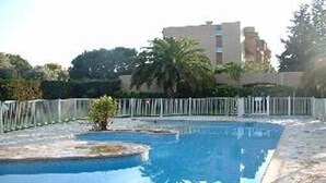 A swimming pool with a clear blue water surface, surrounded by a white fence and palm trees. - Charming, sunny, comfortable, 2 rooms Antibes, very close to the sea ON FOOT (Antibes)
