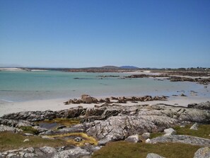 A rocky shoreline with clear turquoise water, a sandy beach, and distant hills. - SUPERB COTTAGE ON 9 ACRES PROPERTY (Oughterard)