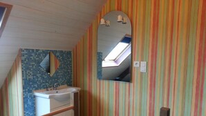 Un baño con pared de azulejos, un lavamanos, un espejo y una ventana.