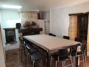 Un espace repas avec une longue table et plusieurs chaises, une petite étagère ornée d’objets décoratifs et un mur en pierre.