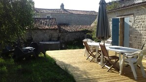 A wooden deck with outdoor furniture, a stone wall, and a tiled roof in the background. - SAINT-SORNIN Atypical house with large plot 900 m2 closed ripe (Saint-Sornin)