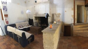 A rustic living room with a fireplace, a sofa, and a coffee table. There is a staircase leading to an upper level. - SAINT-SORNIN Atypical house with large plot 900 m2 closed ripe (Saint-Sornin)