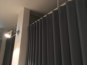 A room with a large window covered by vertical blinds, a wall-mounted light fixture, and a visible ceiling corner. - Guest House Ori Ori (Niigata)