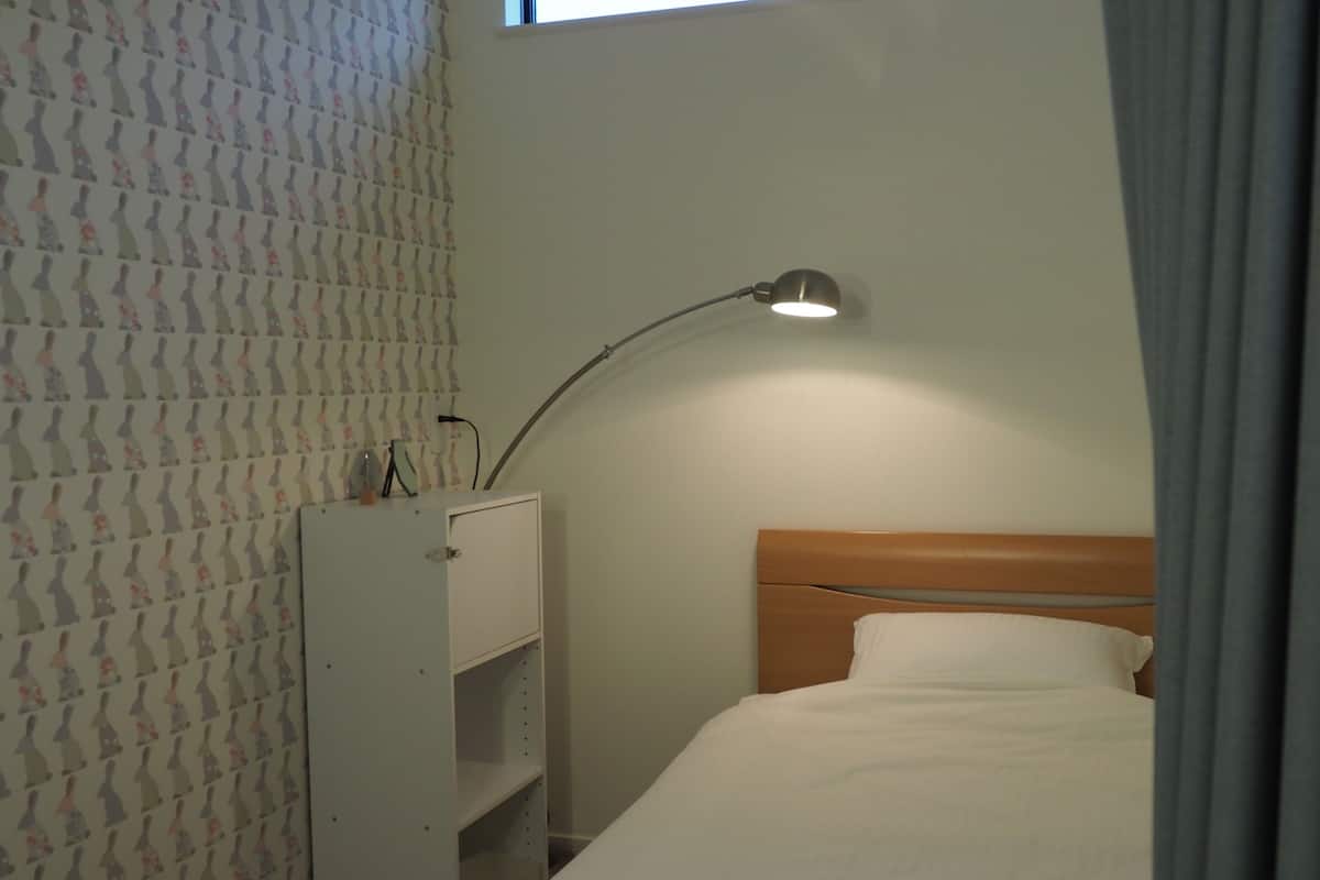 A bedroom with a bed, a nightstand, a desk, and a lamp.