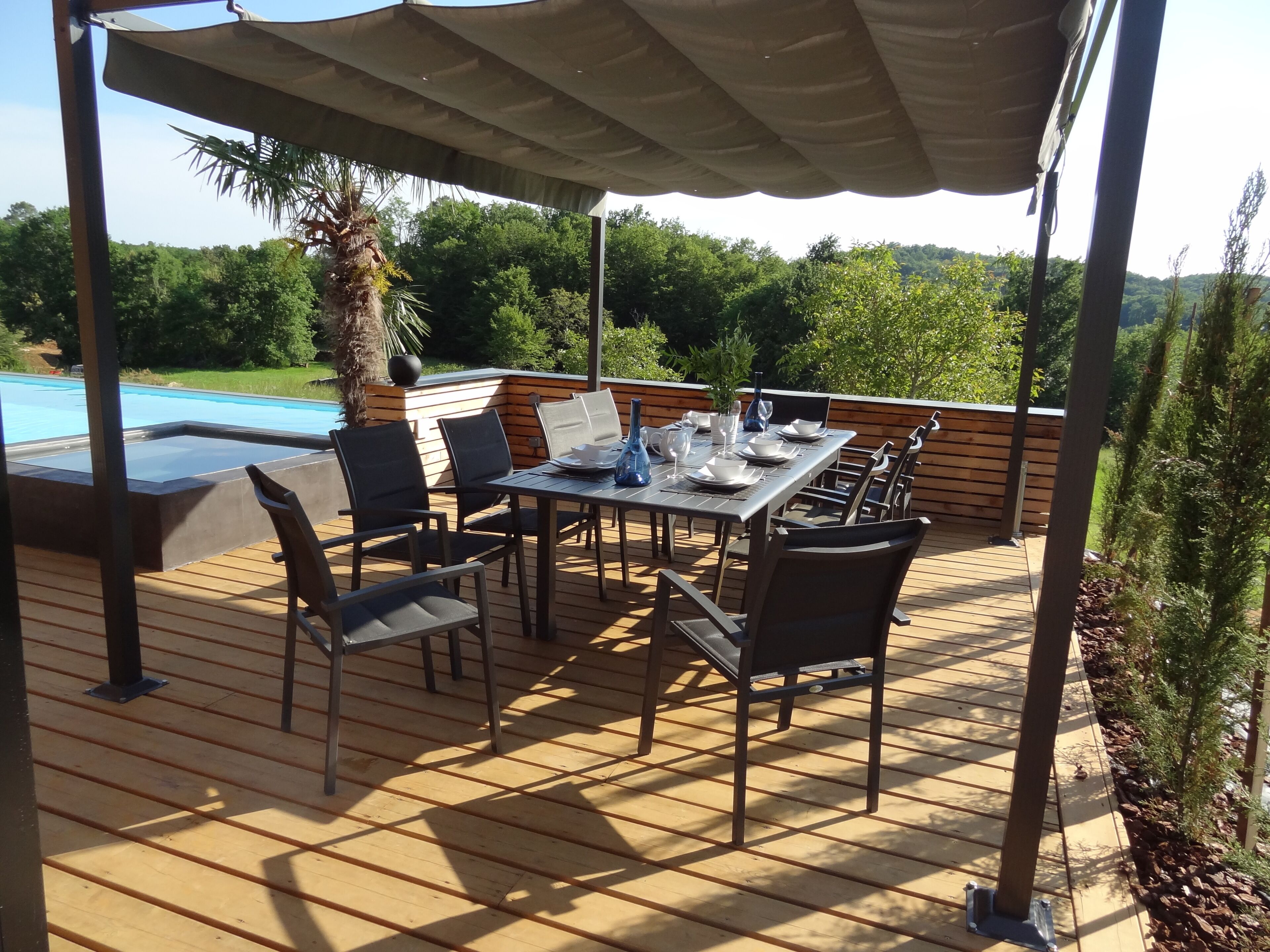 Un patio exterior con una mesa lista para comer, rodeado de sillas y una piscina al fondo.