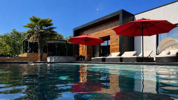 Ein moderner Poolbereich mit Liegestühlen und Sonnenschirmen, umgeben von einer Holzterrasse und Palmen.