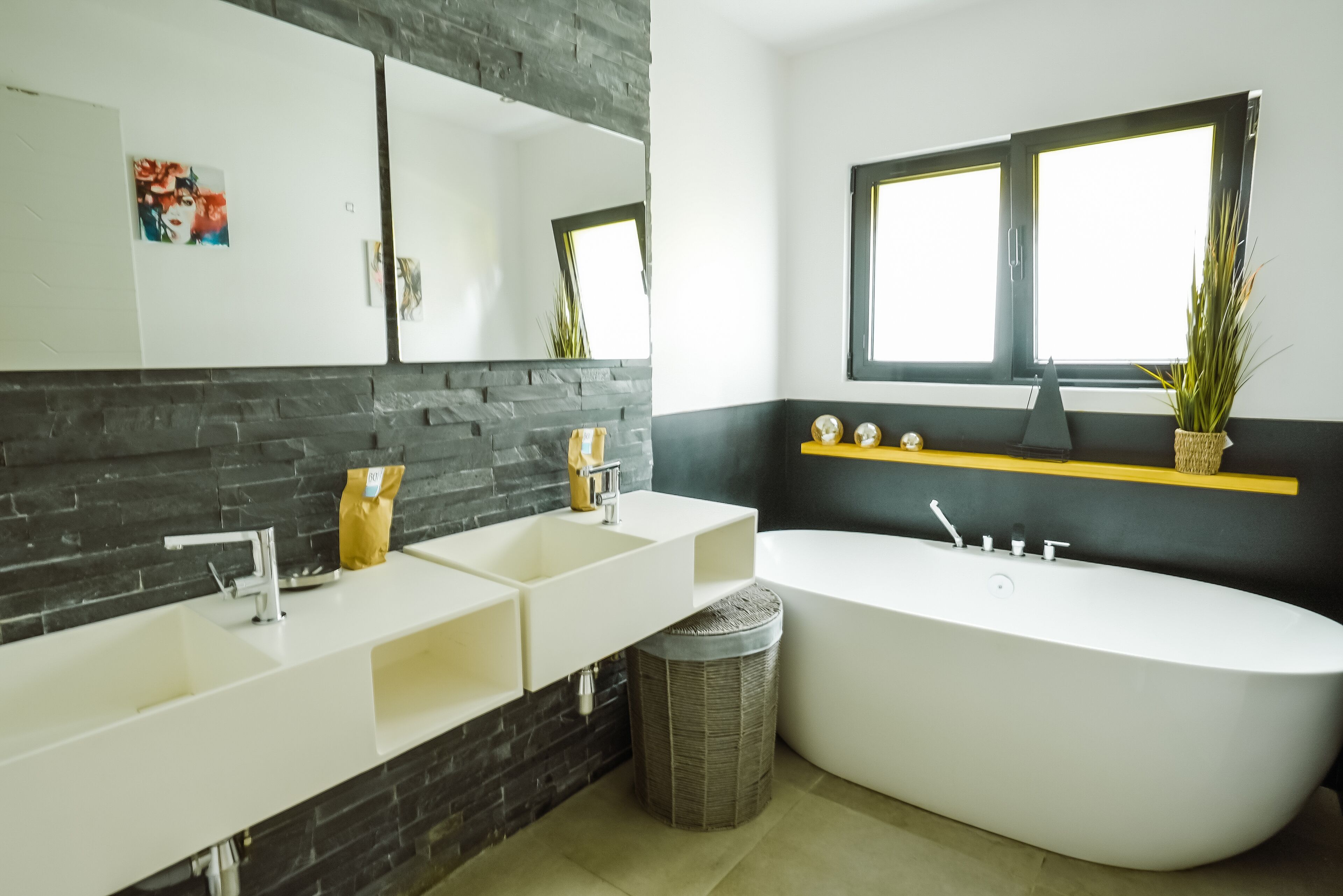A modern bathroom with a double sink, a freestanding bathtub, a large mirror, and a window with a view.
