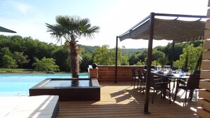 Eine Holzterrasse mit Pool, Sitzgelegenheiten im Freien und einem Esstisch.
