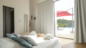 Ein Hotelzimmer mit einem Bett, einem Tablett mit Handtüchern und einem Getränk, einem Fenster mit Vorhängen und Blick auf einen Pool und Bäume.