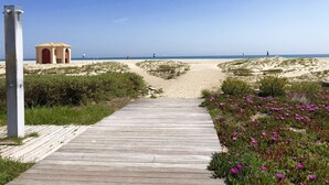 Een houten pad dat naar een strand leidt, met een klein gebouw en duinen.