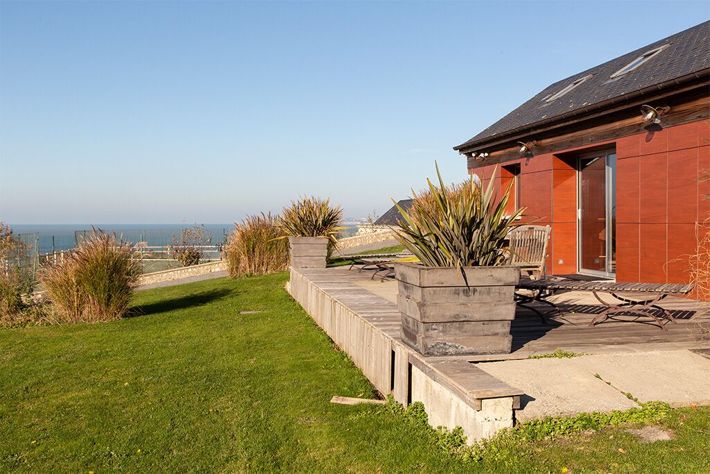 Un bâtiment situé sur la côte, doté d’un patio, d’un bac à fleurs en béton planté et offrant une vue sur la mer.