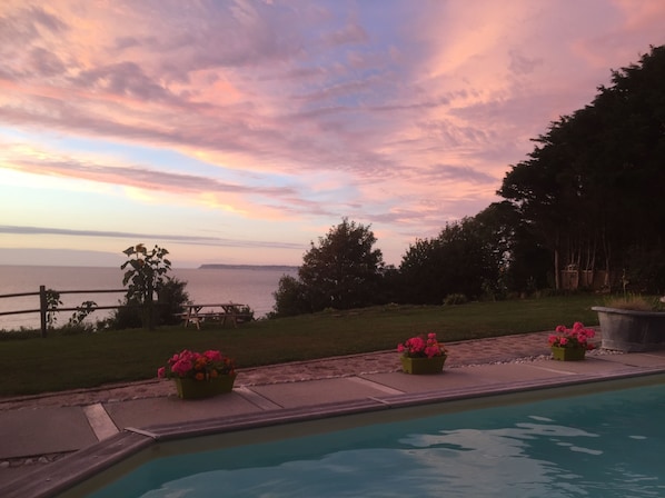 Un espace piscine offrant une vue sur l’océan et un ciel au coucher du soleil.