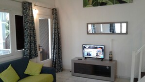 A living room with a sofa, a flat-screen TV on a stand, a mirror above the TV, and a door with patterned curtains. - Nice duplex in Saint François in Guadeloupe (Saint François)