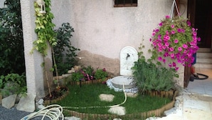 Ein Garten mit Steinmauer, Hängetasche mit Blumen, einer weißen Tür und einem kleinen Teich.