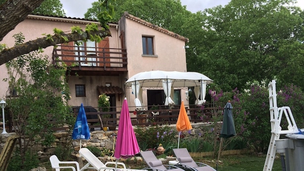 Eine Terrasse mit Gartenmöbeln und Sonnenschirmen, eine Steinmauer und ein Gebäude mit Balkon.