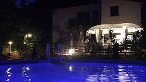 Ein Poolbereich bei Nacht mit überdachter Sitzgelegenheit und einem Gebäude im Hintergrund.