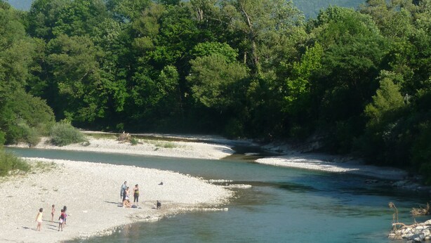 Orilla de río con gente y una montaña al fondo.