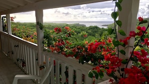 Ein überdachter Balkon mit weißen Geländern und Blick auf das Meer und Grünflächen.