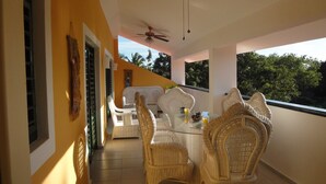 Ein Balkon mit Korbstühlen und einem Tisch, einem Deckenventilator und Blick auf Bäume.